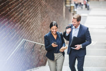 Happy male and female entrepreneurs using phone while climbing staircase in city - MASF16939