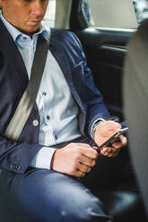 Älterer Geschäftsmann, der im Auto sitzend ein Mobiltelefon benutzt - MASF16954