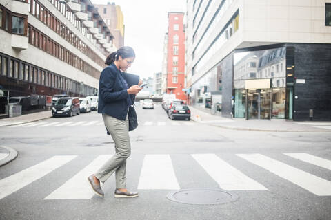 Geschäftsfrau benutzt Mobiltelefon beim Überqueren der Straße, lizenzfreies Stockfoto