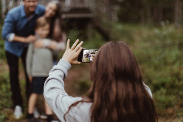 Girl taking picture of family with mobile phone while standing in backyard - MASF17000