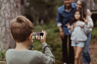 Boy taking picture of family with mobile phone while standing in backyard - MASF17002