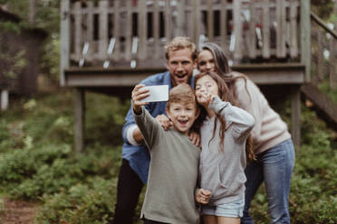 Lächelnde Familie, die ein Selfie mit einem Mobiltelefon macht, während sie vor einem Haus steht - MASF17003