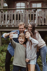 Smiling boy taking selfie with family on mobile phone while standing against house - MASF17004