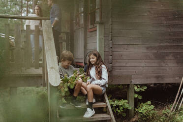 Full length of sibling sitting on doorsteps while parents standing in background - MASF17006