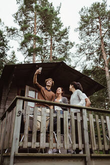 Lächelnde Freunde, die ein Selfie mit ihrem Mobiltelefon machen, während sie in einer Veranda stehen - MASF17034