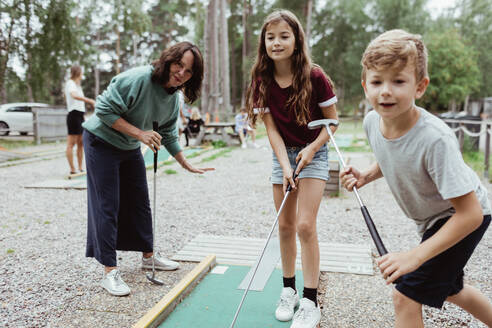 Geschwisterkind spielt im Urlaub mit der Familie im Garten Minigolf - MASF17045