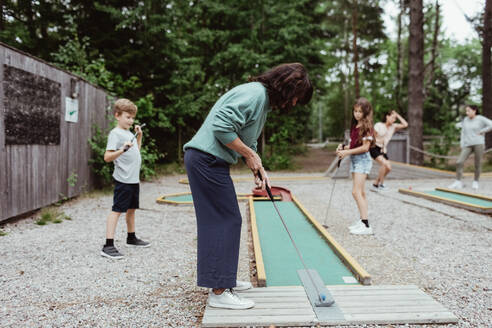 Frau in voller Länge beim Minigolfspielen mit Familie im Hinterhof - MASF17047