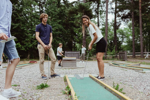 Lächelnde Freunde in voller Länge beim Minigolfspielen im Hinterhof im Urlaub - MASF17048