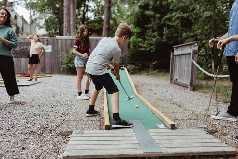 Familie sieht, wie ein Junge beim Minigolfspielen im Hinterhof einen Schuss abgibt - MASF17049