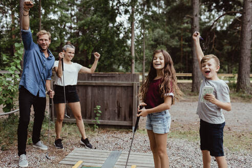 Fröhliche Familie mit erhobenen Armen beim Minigolfspielen im Hinterhof - MASF17050