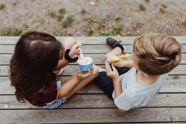 High angle view of siblings eating sweet food while sitting on wooden steps - MASF17057