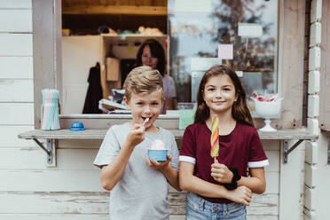 Portrait of sibling eating sweet food while standing against concession stand - MASF17064