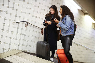 Freundinnen mit Gepäck, die in der U-Bahn stehen und ein Mobiltelefon benutzen - MASF17103