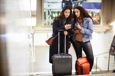 Lesbian couple with luggage using mobile phone while standing in subway - MASF17107