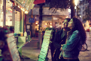 Lesbian couple standing against concession stand in city at night - MASF17116