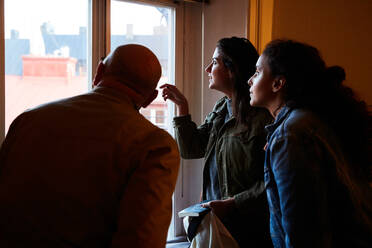 Frauen schauen durch ein Fenster, während sie mit einem männlichen Besitzer zu Hause stehen - MASF17124