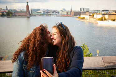 Lächelnde lesbische Paar küssen, während der Einnahme selfie mit Handy gegen Stadtlandschaft - MASF17134