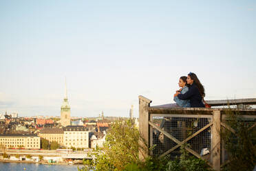 Side view of lesbian couple standing at observation point by cityscape against sky - MASF17140