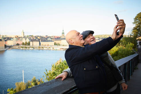 Lächelnde Freunde nehmen Selfie mit Handy gegen Fluss in der Stadt - MASF17144
