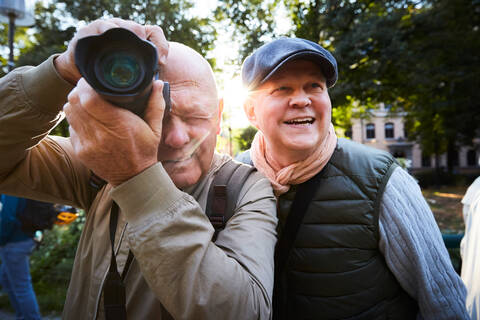 Ein älterer Mann benutzt eine Kamera, während er mit einem Freund in einem Park in der Stadt steht, lizenzfreies Stockfoto