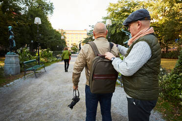 Älterer Mann, der den Gurt der Tasche eines Freundes in einem Park in der Stadt zurechtrückt - MASF17154