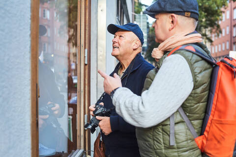 Älteres homosexuelles Paar, das in der Stadt im Urlaub mit der Kamera am Schaufenster steht, lizenzfreies Stockfoto