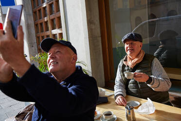 Lächelndes schwules Paar, das ein Selfie mit dem Handy macht, während es in einem Straßencafé sitzt - MASF17172