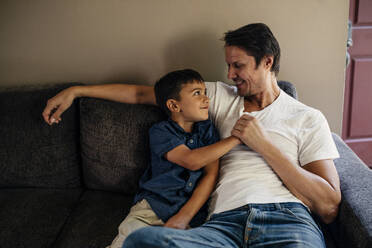 Glücklicher Vater mit Sohn, der zu Hause auf dem Sofa sitzt - MASF17206