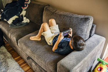 Hoher Blickwinkel eines Jungen, der auf dem Sofa zu Hause liegt und mit seinem Handy spielt - MASF17210