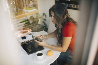 Freelancer female using phone seen through glass window - MASF17215