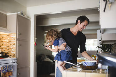 Tochter telefoniert, während der lächelnde Vater in der Küche arbeitet - MASF17220