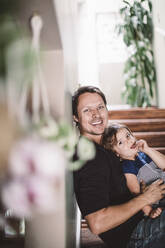 Porträt eines glücklichen Vaters mit seiner Tochter, die zu Hause auf den Stufen sitzt - MASF17225