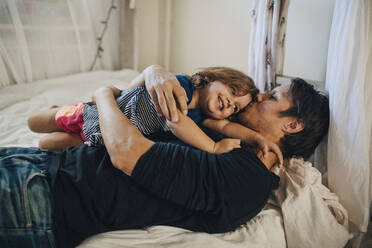 Reifer Vater küsst Tochter auf dem Bett liegend - MASF17244