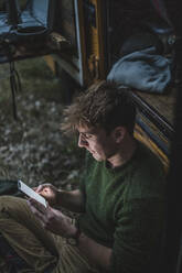 High angle view of male camper using smart phone against motor home during camping - MASF17272