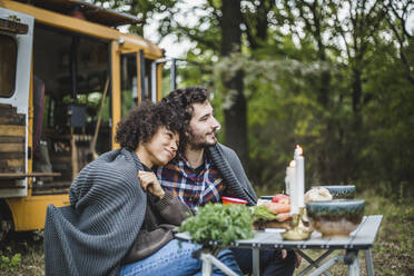 Young multi-ethnic couple wrapped in blanket while sitting at table and looking away - MASF17291