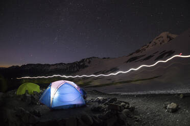 Ein Licht leuchtet aus einem blauen Zelt, während über dem Basislager am Mt. Baker die Sterne leuchten - CAVF76735