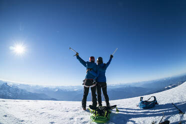 Two happy female mountaineers raise their ice axes in victory - CAVF76739