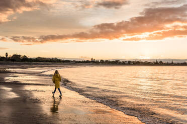 Mädchen spaziert am neuseeländischen Strand bei Sonnenuntergang - CAVF76754