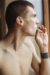 A side profile close-up portrait of a young man smoking cigarette - CAVF76772