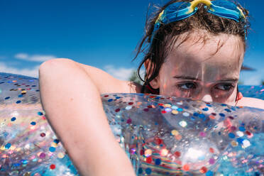 Nahaufnahme eines traurig aussehenden Mädchens, das mit einer Schwimmbrille auf dem Kopf im Pool schwimmt - CAVF76826