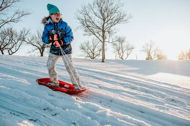 Actionshot eines Mädchens, das auf einem Schlitten steht und im Winter einen Hügel hinunterfährt. - CAVF76827