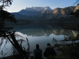 Two friends in the early morning by still lake in the Rocky Mountains - CAVF76845