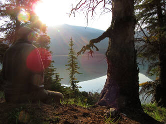 Junger Mann meditiert allein an einem stillen Bergsee bei Sonnenaufgang - CAVF76846