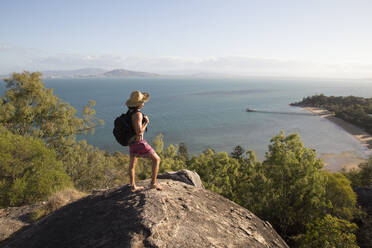 Backpacker with hat and swimsuit, on top of rocky hill during sunset - CAVF76888