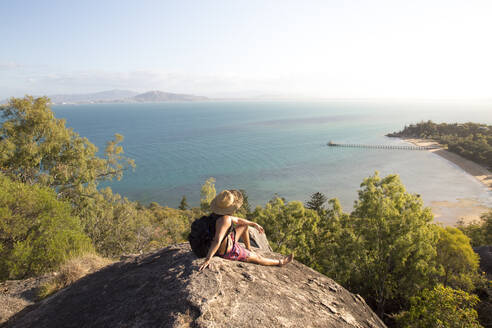 Backpacker with hat and swimsuit, on top of rocky hill during sunset - CAVF76890