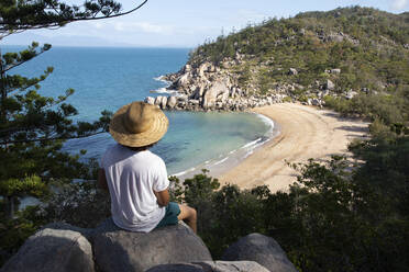 Mann mit lockigem Haar, Hut und Badeanzug, auf einem Felsen, die Bucht bewundernd - CAVF76892