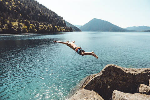 Seitenansicht eines jungen Mannes, der in einen Alpensee vor den Bergen springt, lizenzfreies Stockfoto