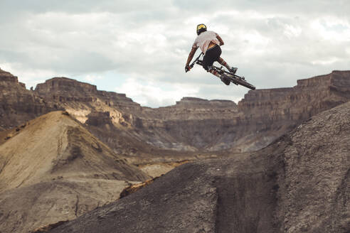 Rückansicht eines jungen Mannes, der mit einem Mountainbike durch eine Wüstenlandschaft springt - CAVF76959