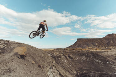 Male jumping with mountain bike in front of dramatic mountains - CAVF76961