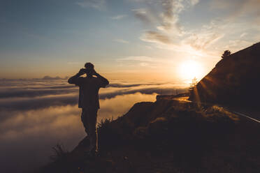 Young Male photographing sunset above clouds next to highway - CAVF76964